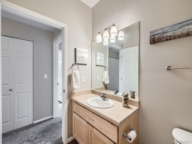 bathroom featuring toilet, a textured wall, vanity, and baseboards