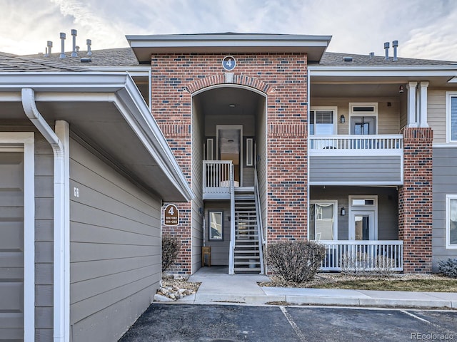 view of exterior entry with brick siding, a shingled roof, and a balcony