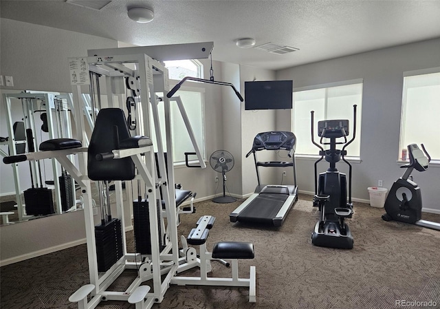 exercise room featuring visible vents, a textured ceiling, and baseboards