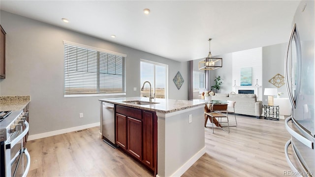 kitchen featuring a large fireplace, sink, light stone counters, pendant lighting, and appliances with stainless steel finishes