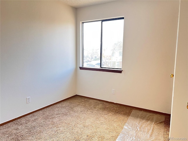 empty room with carpet flooring, a textured ceiling, and baseboards