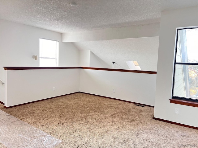 carpeted empty room featuring lofted ceiling, visible vents, a textured ceiling, and baseboards