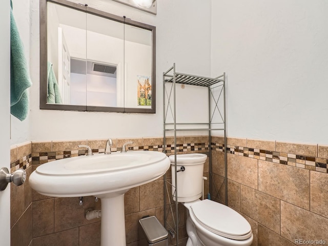 half bath with toilet, tile walls, and wainscoting