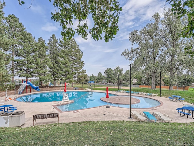 community pool with a lawn, fence, a water slide, playground community, and a patio area