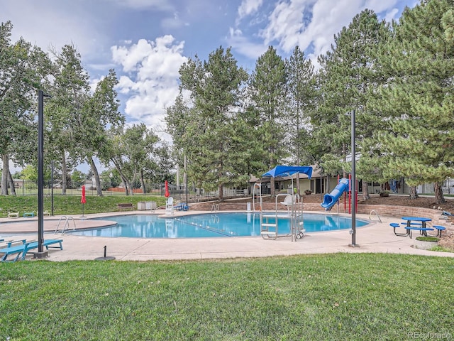 community pool with a yard, a water slide, playground community, and fence