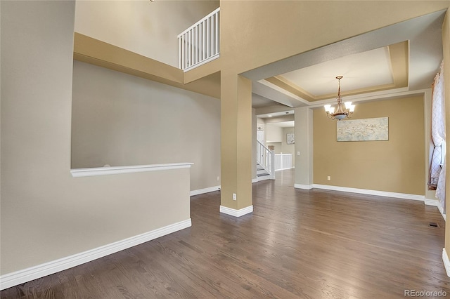 unfurnished room with wood finished floors, baseboards, stairway, a raised ceiling, and an inviting chandelier