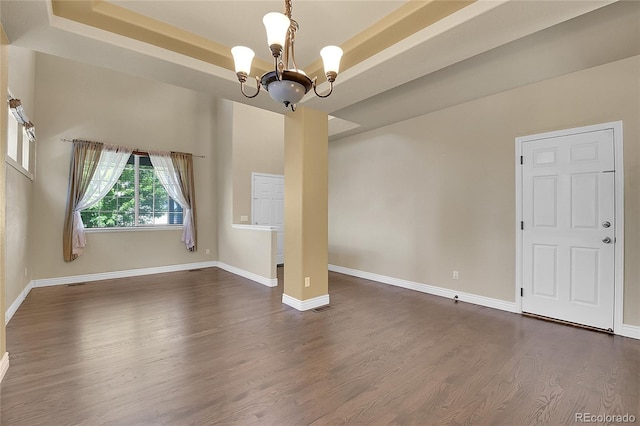 unfurnished dining area with baseboards, a chandelier, dark wood finished floors, and a raised ceiling