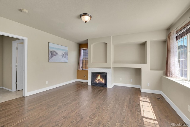 unfurnished living room featuring baseboards, visible vents, dark wood finished floors, and a tiled fireplace