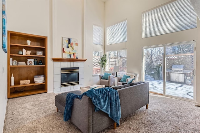 living room with built in shelves, a tile fireplace, carpet, and a high ceiling