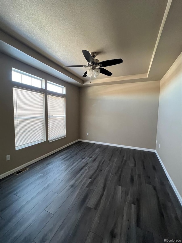 spare room with a textured ceiling, dark hardwood / wood-style flooring, a raised ceiling, and ceiling fan