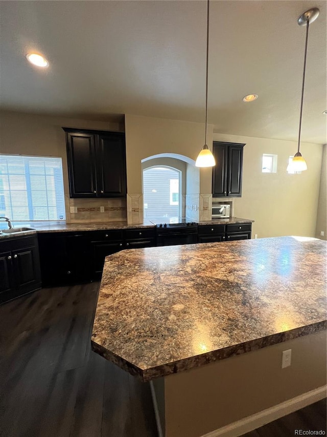 kitchen featuring dark hardwood / wood-style flooring, backsplash, sink, a center island, and hanging light fixtures