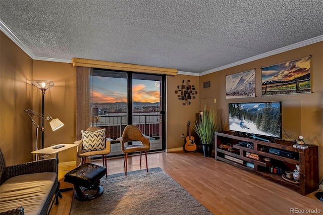 living area with a textured ceiling, wood finished floors, visible vents, and ornamental molding