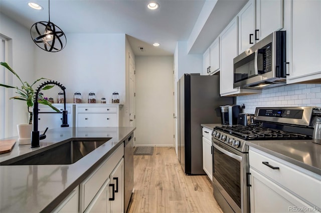 kitchen featuring a sink, white cabinets, light wood-style floors, appliances with stainless steel finishes, and decorative backsplash