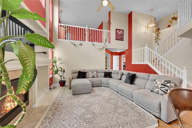 living room with ceiling fan, a towering ceiling, hardwood / wood-style floors, and a tile fireplace