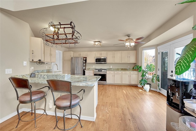 kitchen with light stone counters, stainless steel appliances, a breakfast bar, kitchen peninsula, and light hardwood / wood-style flooring