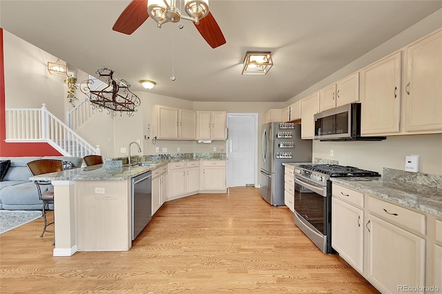 kitchen featuring kitchen peninsula, stainless steel appliances, a breakfast bar, light stone countertops, and light hardwood / wood-style floors