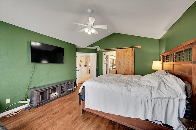 bedroom featuring ceiling fan, connected bathroom, hardwood / wood-style floors, a barn door, and vaulted ceiling