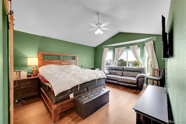 bedroom featuring light hardwood / wood-style floors, vaulted ceiling, a textured ceiling, and ceiling fan