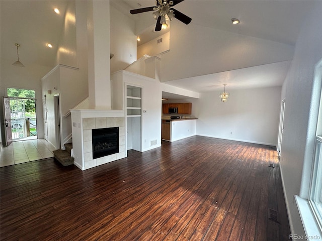 15555 E 40th Ave Unit 11, Denver, CO 80239 - unfurnished living room with high vaulted ceiling, a tiled fireplace, dark wood-style floors, a ceiling fan, and a chandelier