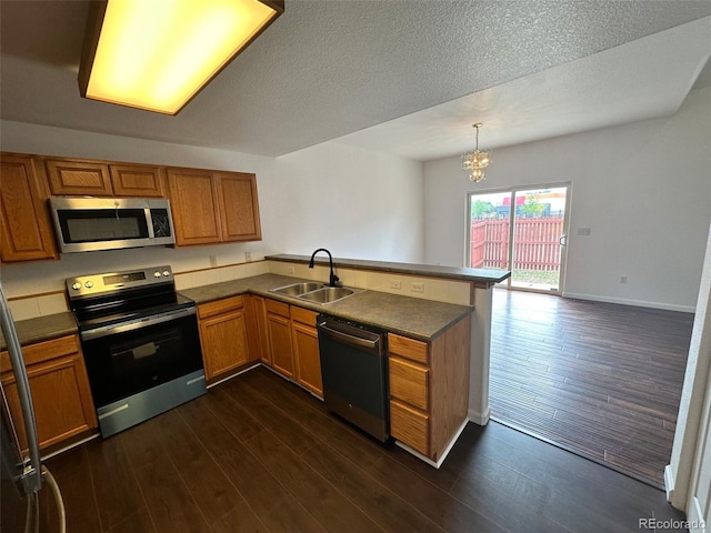 15555 E 40th Ave Unit 11, Denver, CO 80239 - kitchen with appliances with stainless steel finishes, a peninsula, dark wood-style flooring, brown cabinetry, and a textured ceiling