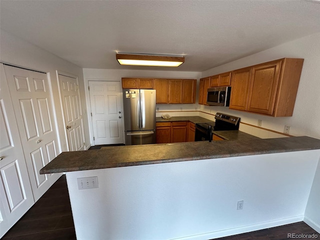 15555 E 40th Ave Unit 11, Denver, CO 80239 - kitchen with appliances with stainless steel finishes, brown cabinetry, a peninsula, dark countertops, and dark wood-type flooring