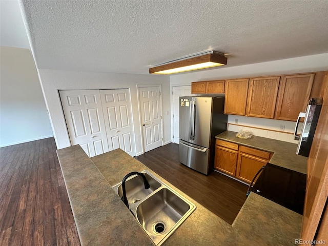 15555 E 40th Ave Unit 11, Denver, CO 80239 - kitchen featuring freestanding refrigerator, dark countertops, dark wood finished floors, brown cabinetry, and a textured ceiling