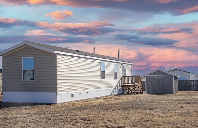 back of property at dusk featuring fence, a storage unit, and an outbuilding