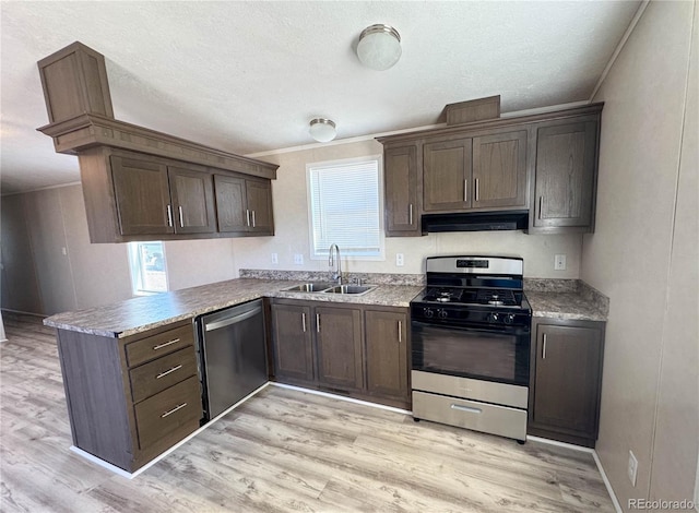 kitchen featuring a peninsula, stainless steel appliances, light wood-style floors, a sink, and exhaust hood