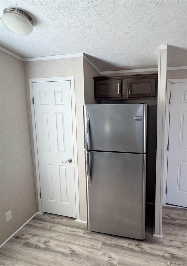 kitchen with dark brown cabinetry, freestanding refrigerator, crown molding, a textured ceiling, and light wood-style floors