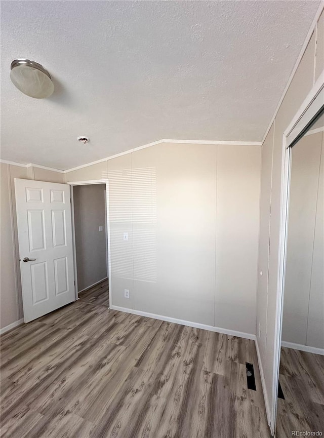 empty room with ornamental molding, a textured ceiling, and wood finished floors