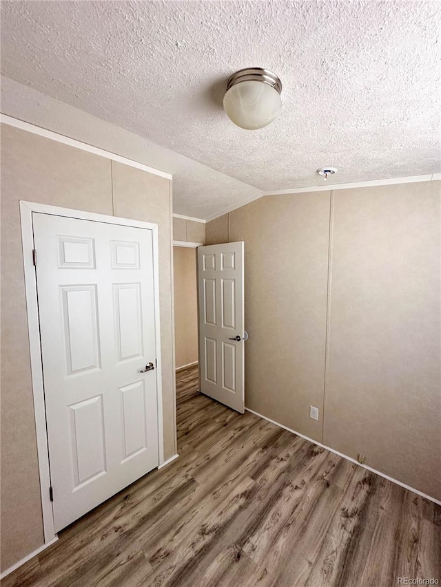 unfurnished bedroom featuring a textured ceiling, ornamental molding, vaulted ceiling, and wood finished floors