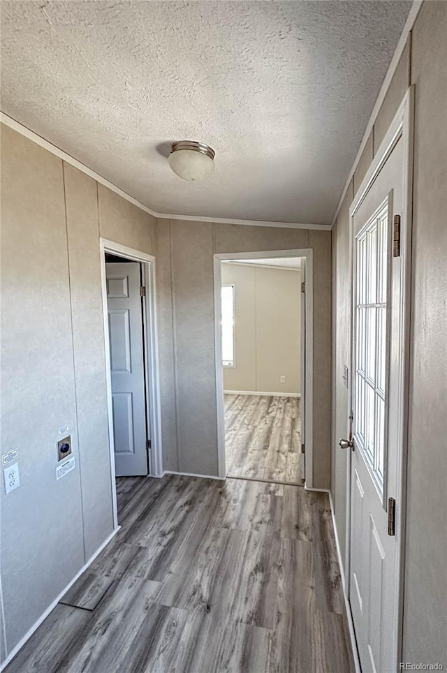 hallway featuring a textured ceiling, ornamental molding, and wood finished floors