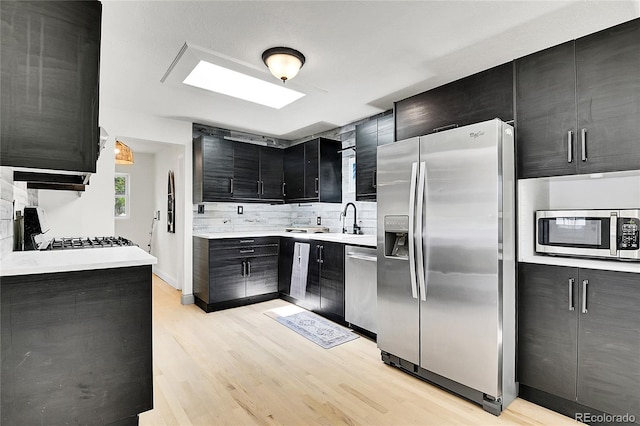 10887 Goodheart Ave, Conifer, CO 80433 - kitchen with appliances with stainless steel finishes, dark cabinets, tasteful backsplash, light wood finished floors, and a sink