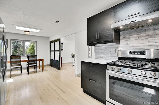 10887 Goodheart Ave, Conifer, CO 80433 - kitchen with stainless steel appliances, extractor fan, dark cabinetry, light countertops, and light wood-style floors