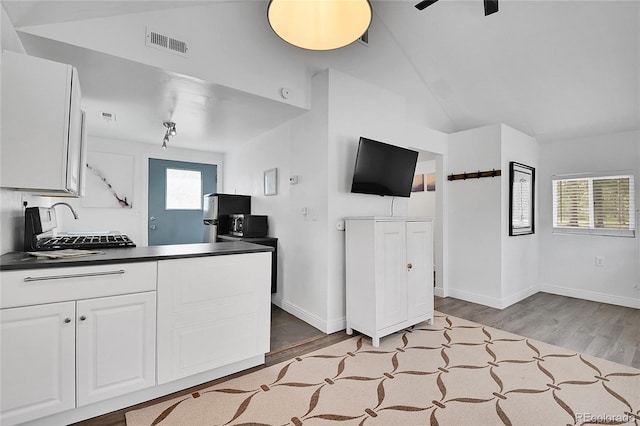10887 Goodheart Ave, Conifer, CO 80433 - kitchen featuring dark countertops, wood finished floors, white cabinetry, vaulted ceiling, and baseboards