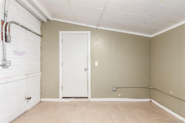 1151 Revere St, Aurora, CO 80011 - empty room with crown molding, brick wall, vaulted ceiling, and light tile patterned flooring