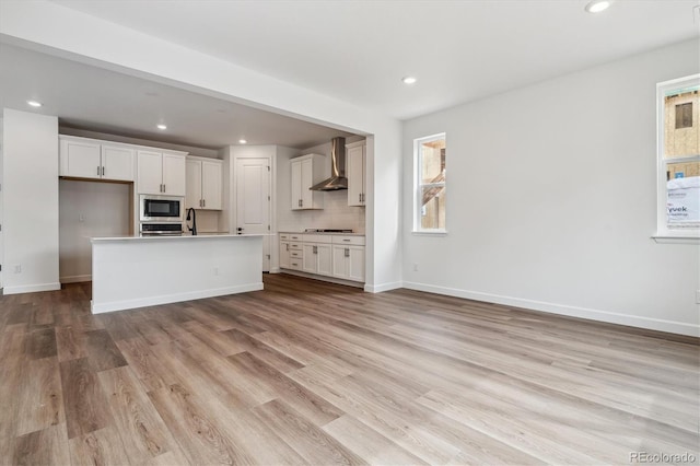 8462 Eagle River St, Littleton, CO 80125 - kitchen featuring white cabinets, baseboards, stainless steel microwave, wall chimney exhaust hood, and light wood-style floors