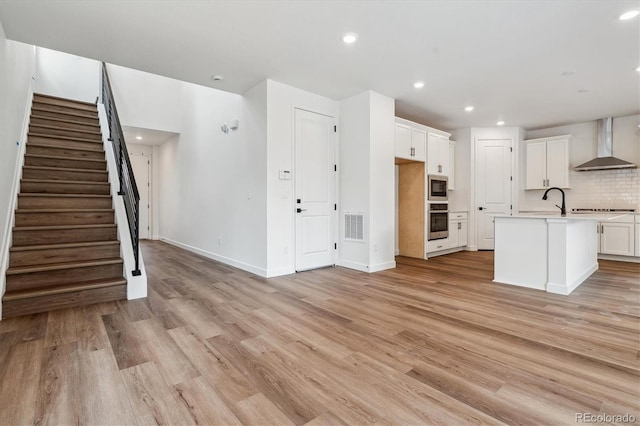 8462 Eagle River St, Littleton, CO 80125 - kitchen featuring white cabinets, light wood finished floors, wall chimney exhaust hood, tasteful backsplash, and appliances with stainless steel finishes
