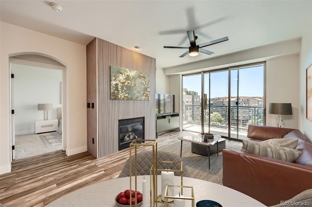 9079 E Panorama Cir Unit 419, Englewood, CO 80112 - living room featuring wood finished floors, ceiling fan, a glass covered fireplace, baseboards, and arched walkways