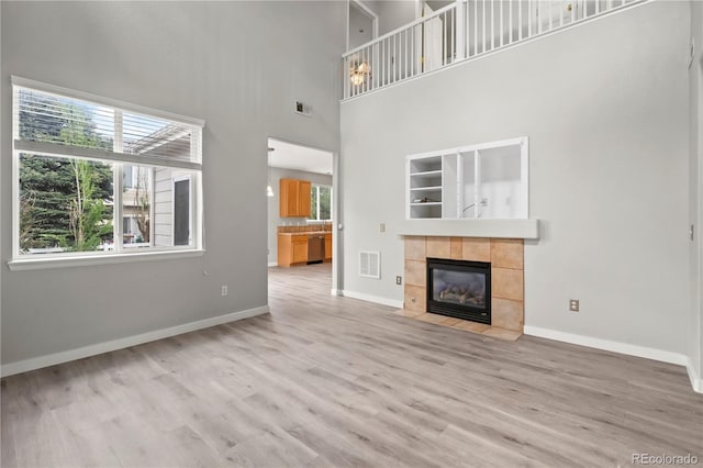 1160 S Fultondale Ct, Aurora, CO 80018 - unfurnished living room with wood finished floors, a tiled fireplace, a towering ceiling, and baseboards