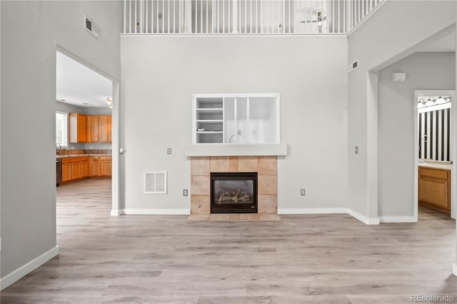 1160 S Fultondale Ct, Aurora, CO 80018 - unfurnished living room featuring a towering ceiling, light wood-style floors, baseboards, and a tiled fireplace
