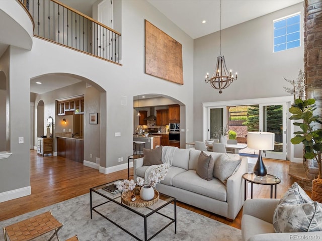 6995 S Ensenada St, Aurora, CO 80016 - living room featuring arched walkways, a towering ceiling, healthy amount of natural light, wood finished floors, and a chandelier