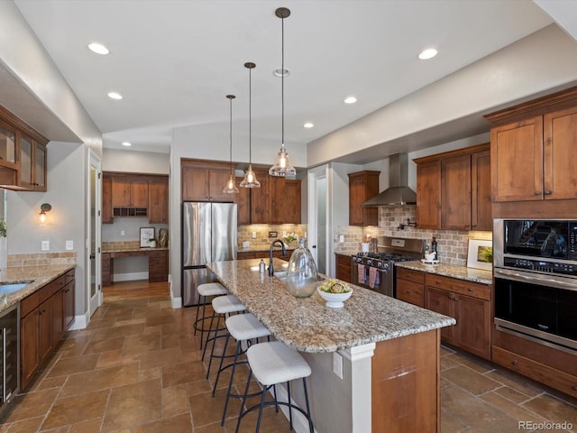 6995 S Ensenada St, Aurora, CO 80016 - kitchen featuring appliances with stainless steel finishes, wall chimney exhaust hood, a breakfast bar area, decorative backsplash, and an island with sink