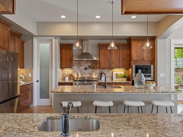 6995 S Ensenada St, Aurora, CO 80016 - kitchen with freestanding refrigerator, wall chimney range hood, range, brown cabinets, and a kitchen bar