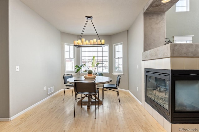 dining area with a chandelier, a tile fireplace, and light wood-type flooring