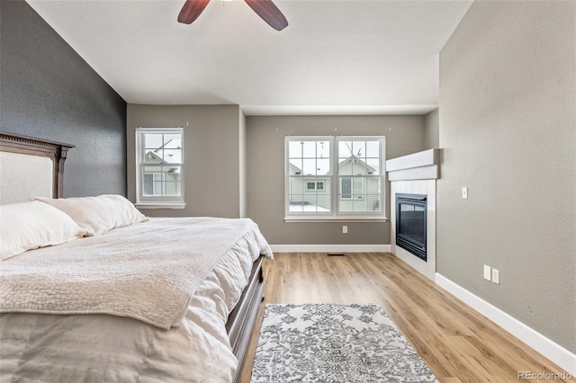 bedroom featuring a fireplace, light hardwood / wood-style flooring, and ceiling fan