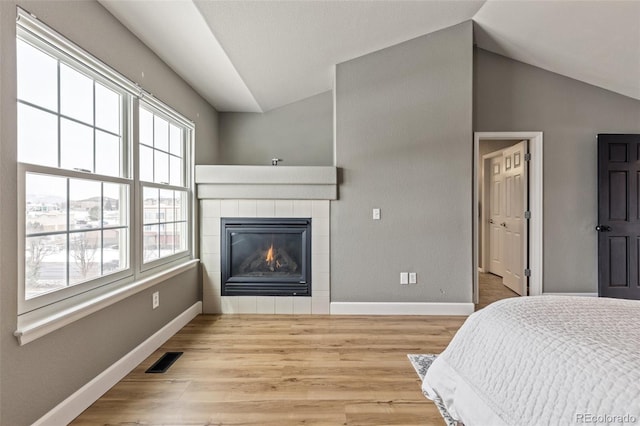 bedroom with a tiled fireplace, lofted ceiling, and light hardwood / wood-style flooring