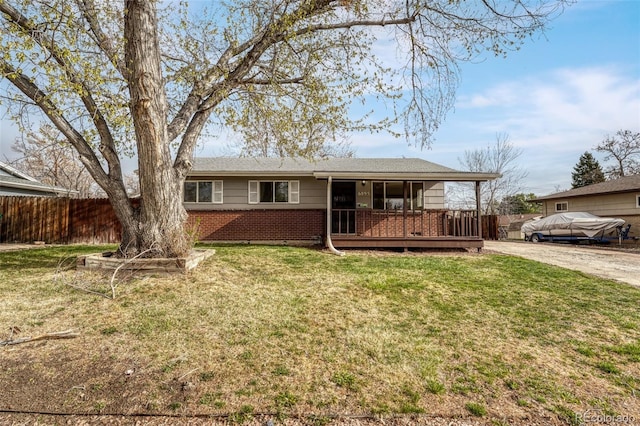 view of front facade with a front yard, brick siding, driveway, and fence