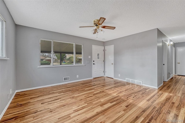 empty room with a textured ceiling, light wood finished floors, a ceiling fan, and visible vents