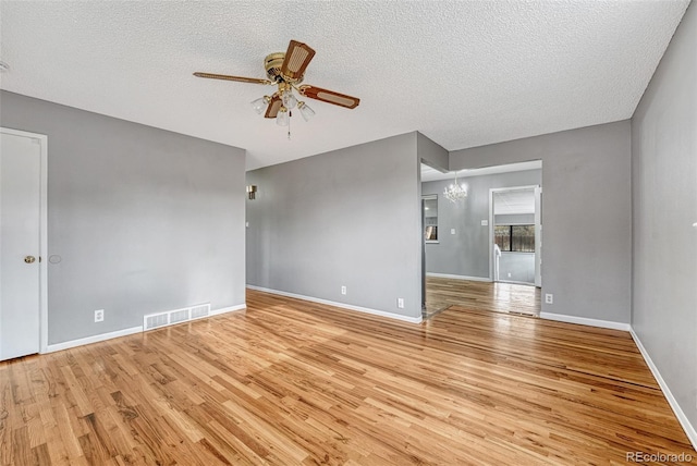 spare room with visible vents, baseboards, light wood-type flooring, a textured ceiling, and ceiling fan with notable chandelier